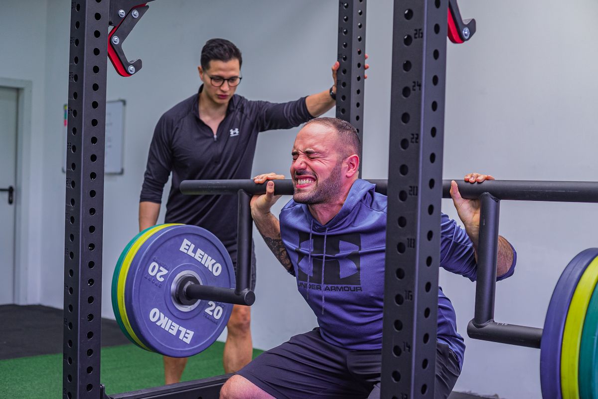 Athlete performing a heavy barbell squat with a coach spotting