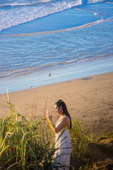 A woman in a white dress takes photos on a beach in Pacifica, CA, USA.