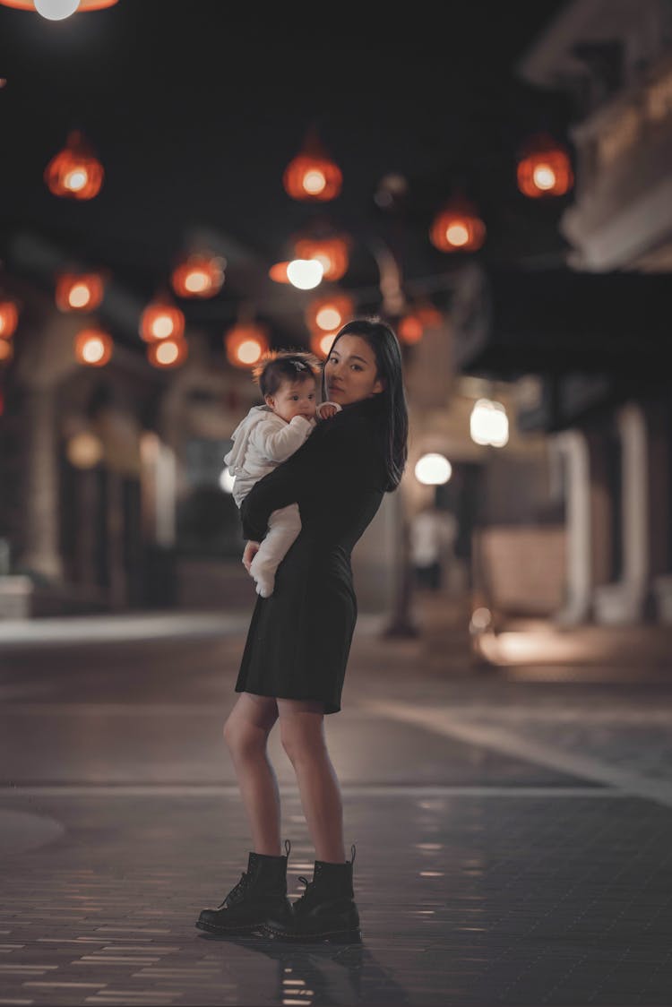 Asian Woman With Kid On Hands Standing On Night Street