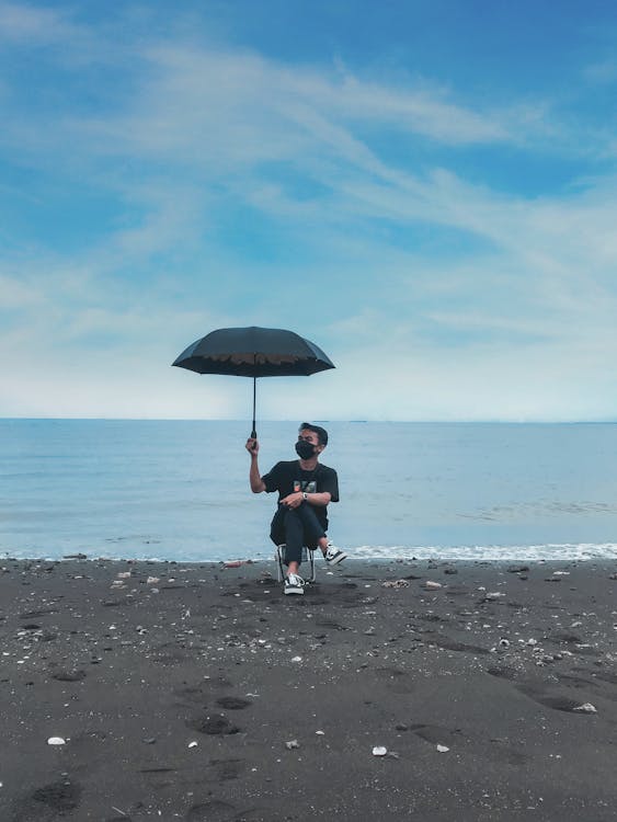 A Man Sitting on the Beach while Holding an Umbrella