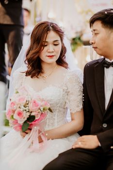 Bride and groom in wedding attire share a moment, holding pink roses.