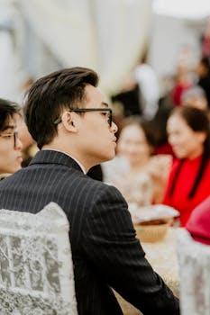 Side view of an Asian man in glasses attending a formal indoor event. Elegant ambiance.