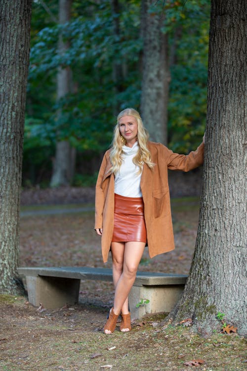 Free Full length of middle aged female in trendy outfit looking at camera while standing in park leaning on tree Stock Photo