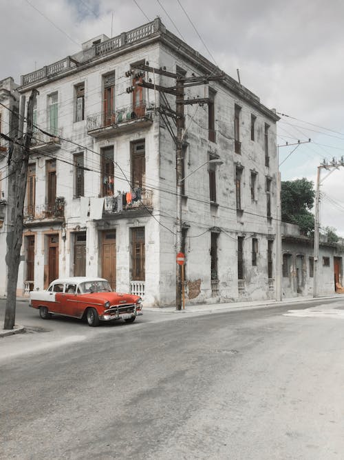 Exterior of old shabby apartment house and parked vintage automobile near wide asphalt roadway in overcast weather