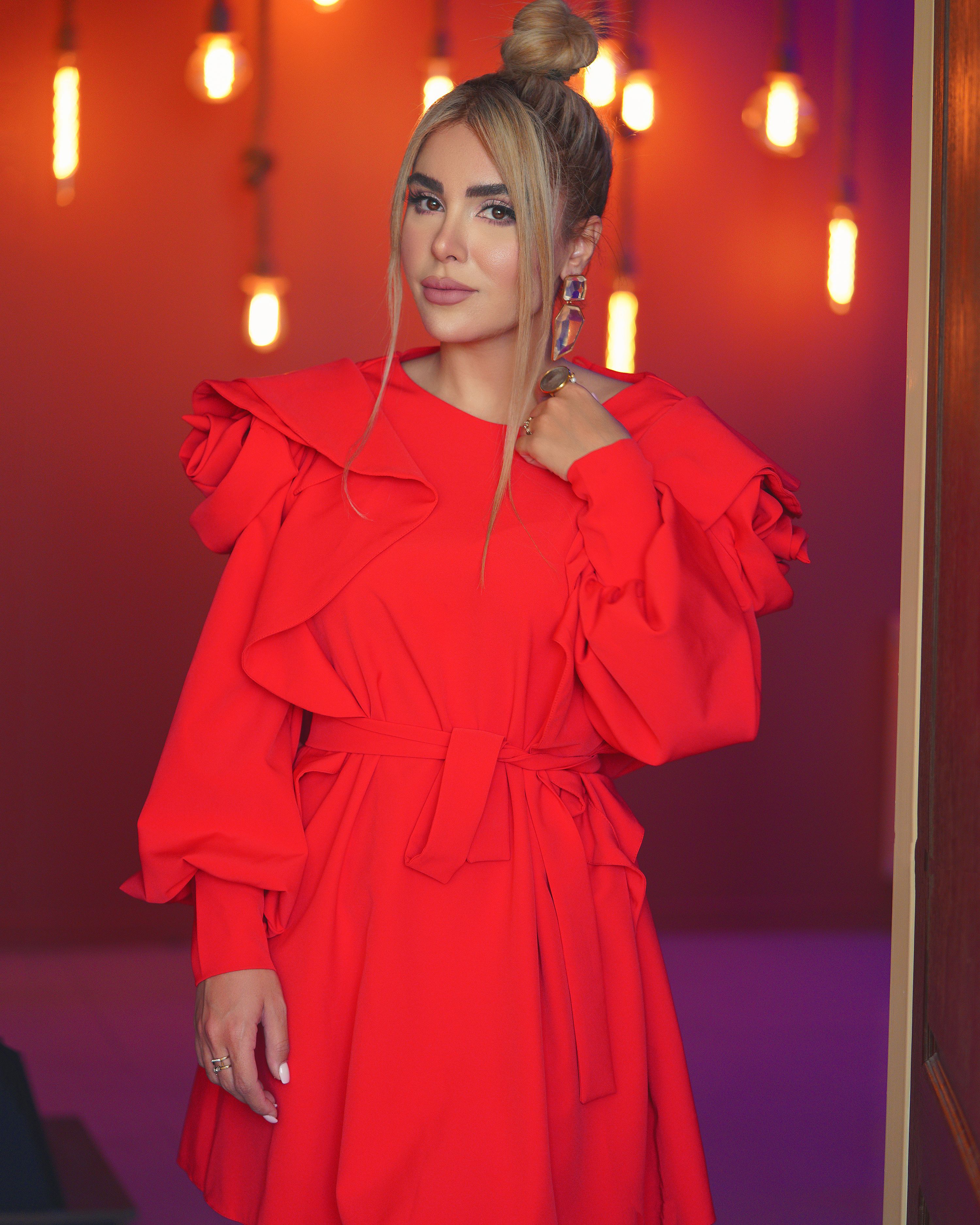 Stylish adult woman wearing a vibrant red dress, posing with warm lighting in Tehran.