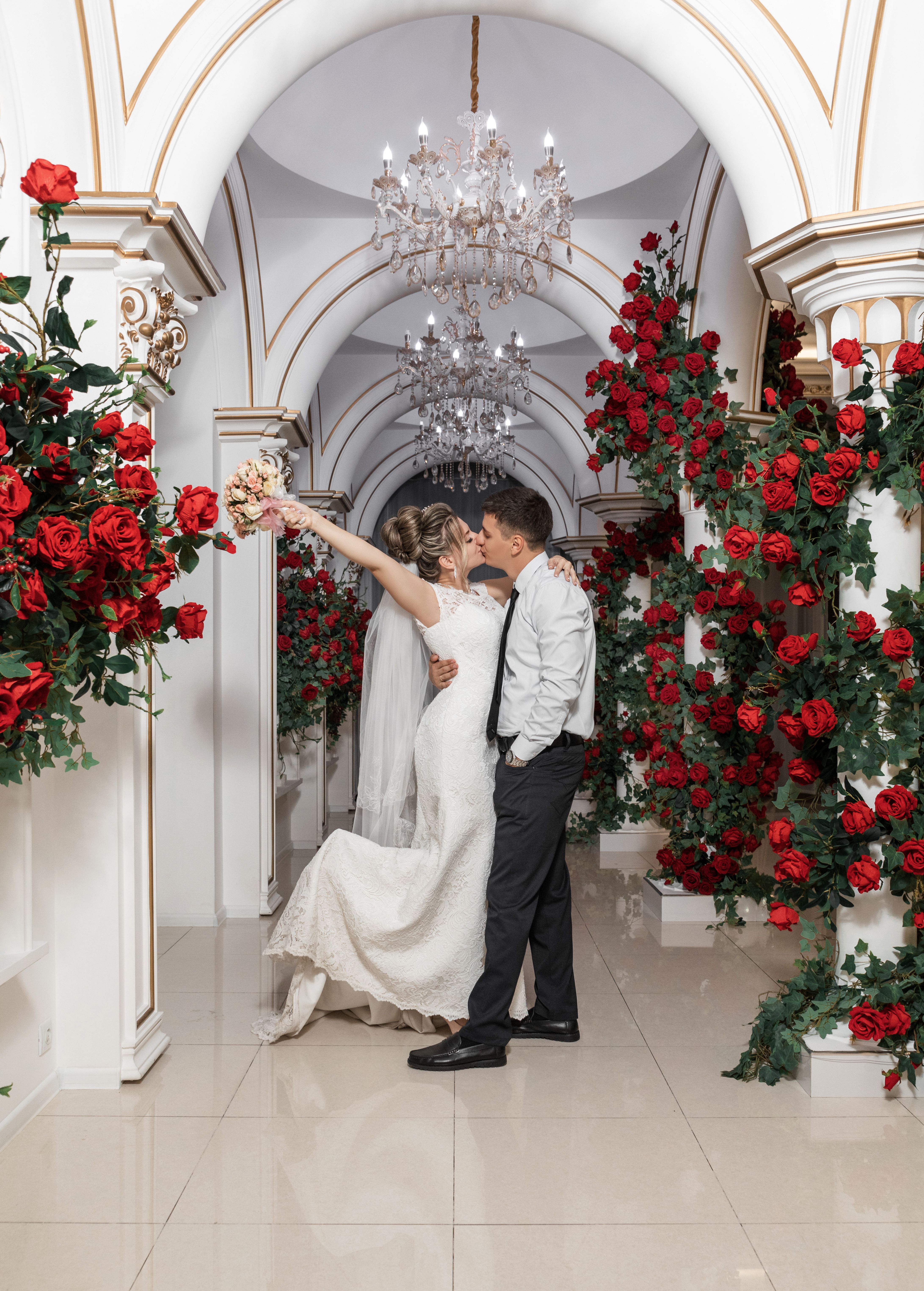 在奢华的走廊里，优雅的新娘和新郎用红玫瑰庆祝婚礼，深情亲吻