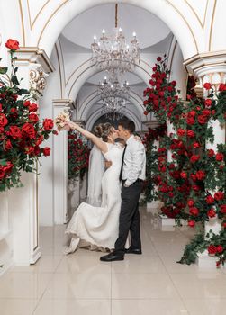 在奢华的走廊里，优雅的新娘和新郎用红玫瑰庆祝婚礼，深情亲吻