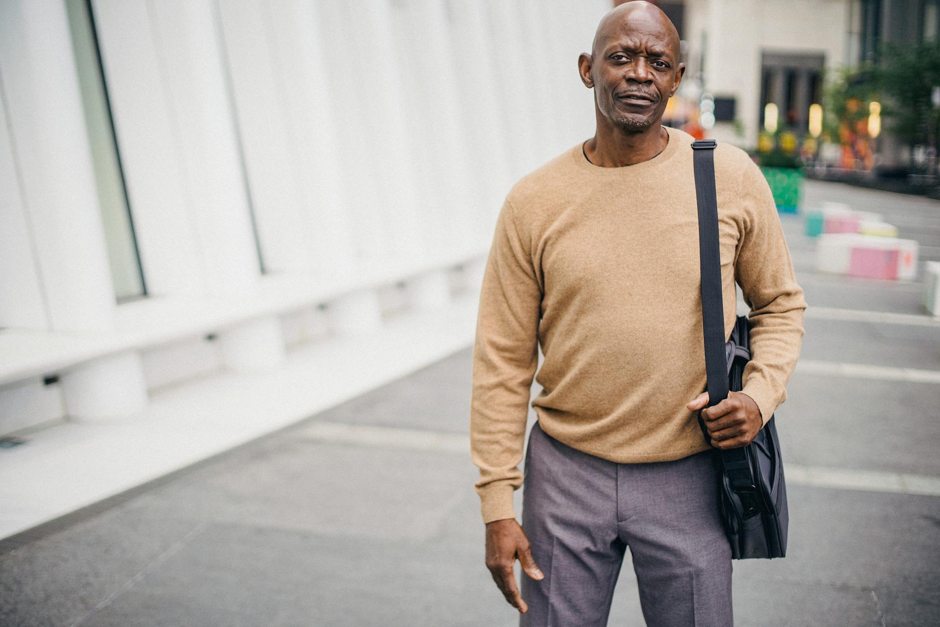 Adult African American businessman in elegant jersey carrying bag looking at camera on street