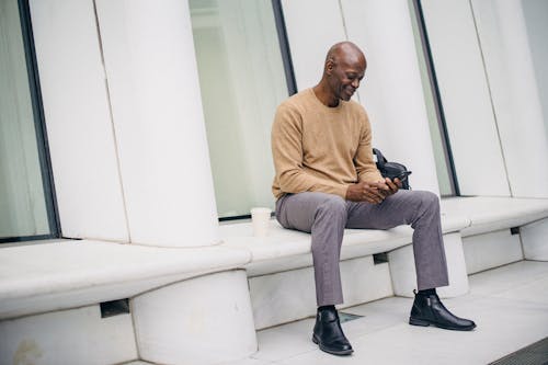 Smiling black businessman using phone on street bench
