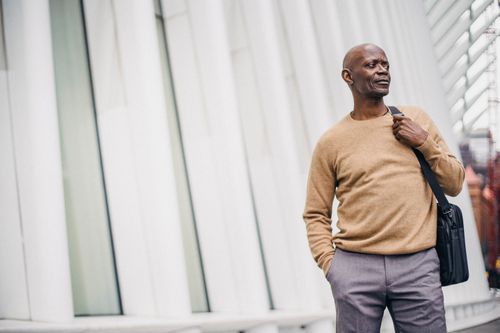 Free Adult African American bald man in jersey holding bag and standing with hand in pocket looking away on street in center Stock Photo