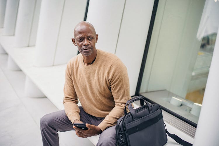 Serious Black Man With Phone On City Bench