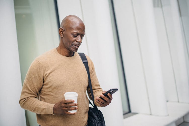 Serious Black Man With Smartphone And Takeaway Coffee