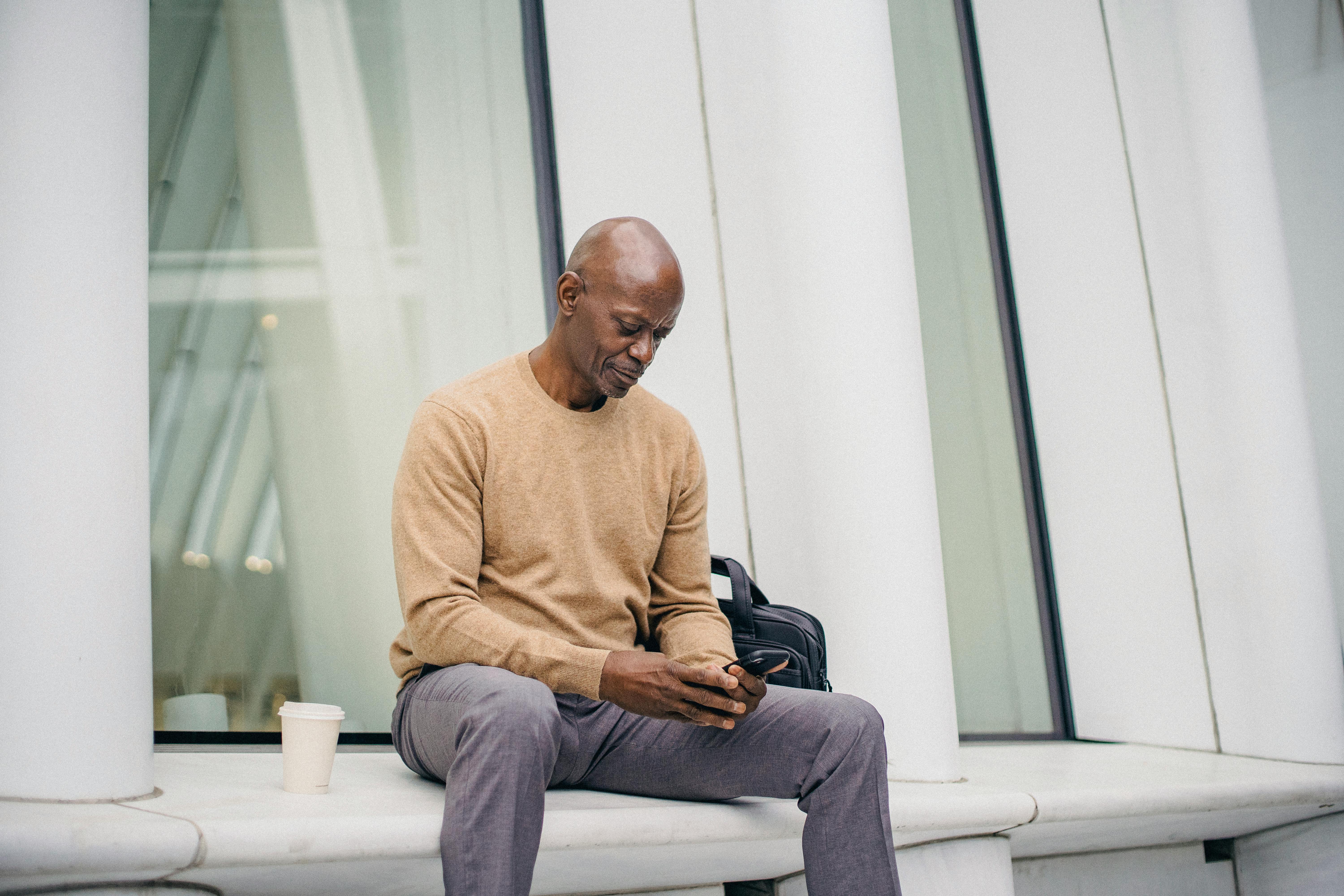 focused black man using mobile phone on bench