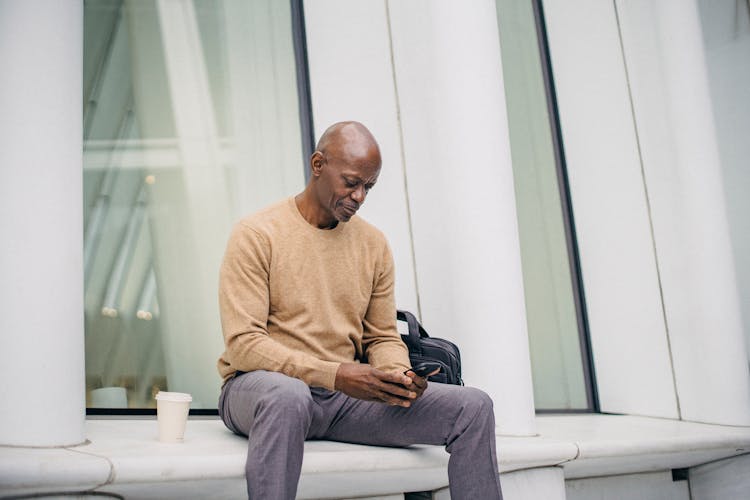 Focused Black Man Using Mobile Phone On Bench