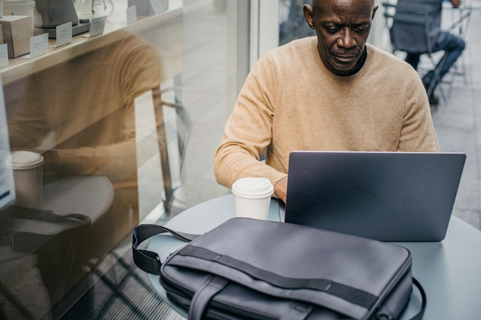 Mature African American man working remotely in a café with a laptop and coffee.