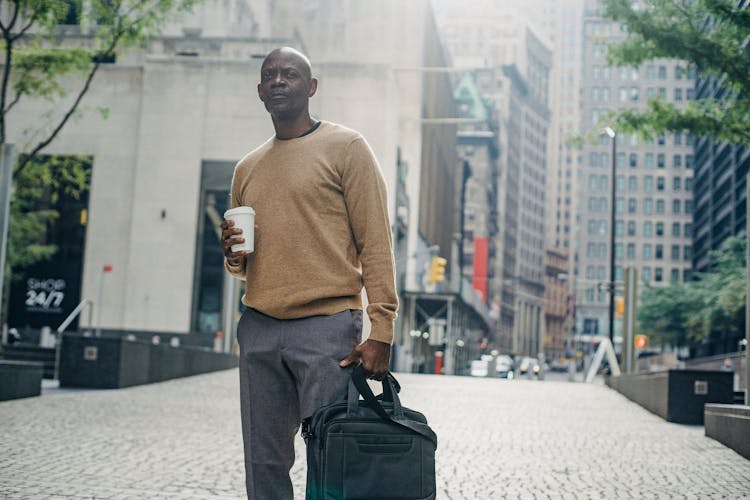 Focused Black Businessman With Coffee And Bag In City