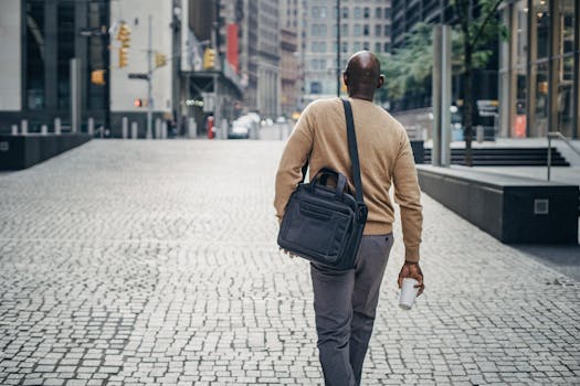 A businessman carrying a bag and coffee walks through a modern city street.