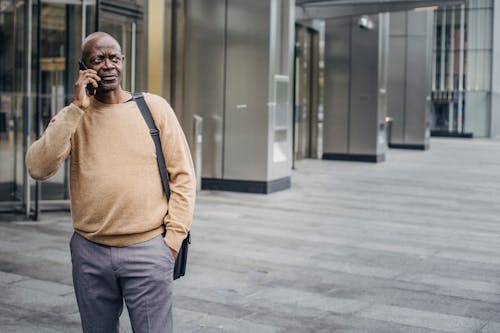 Free Focused African American man with hand in pocket chatting on mobile phone standing in downtown center Stock Photo