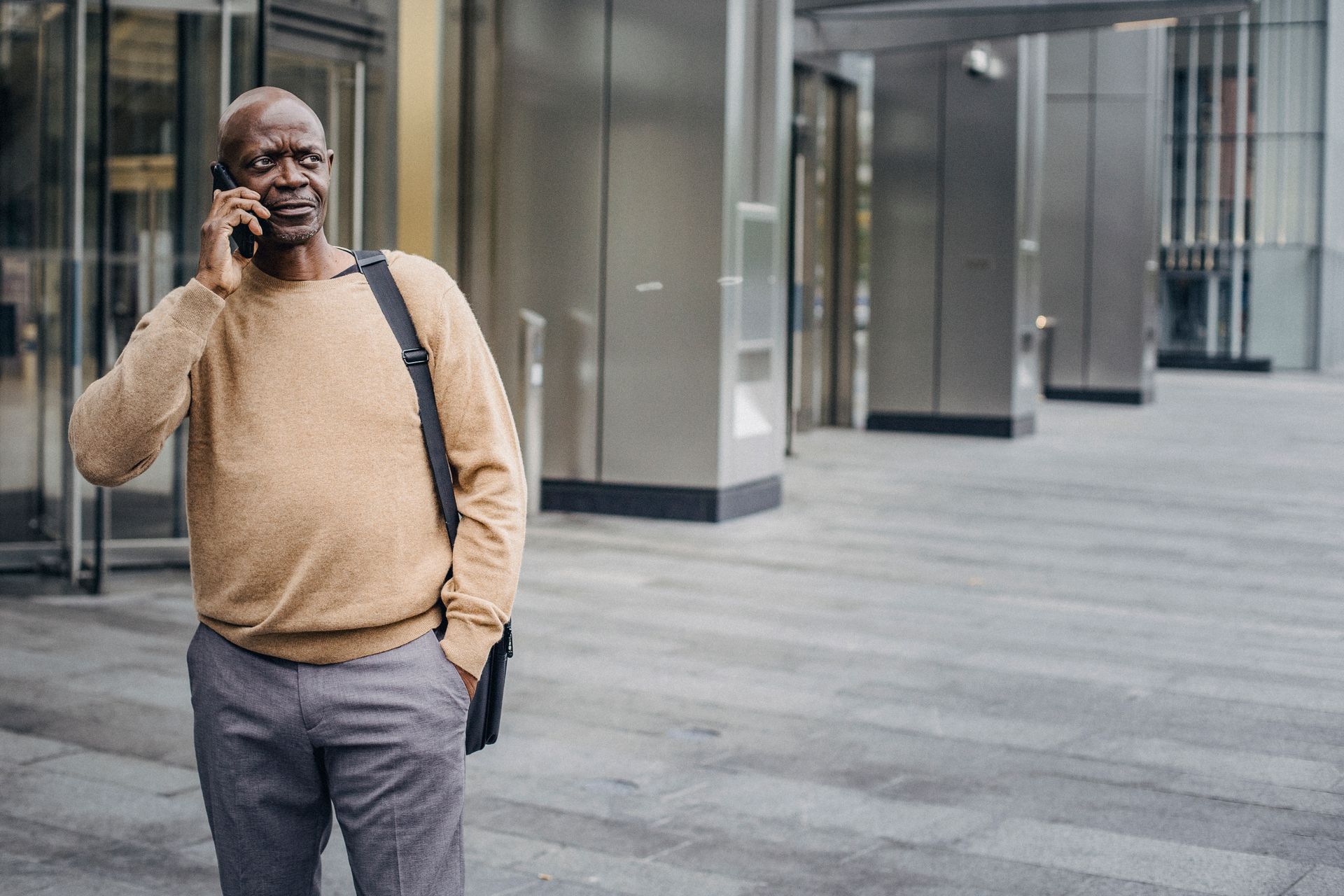 Focused African American man with hand in pocket chatting on mobile phone standing in downtown center
