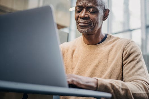 Senior man focused on working remotely using laptop in urban office.