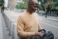 Frowning black businessman with personal case looking inside and grimacing while standing in street