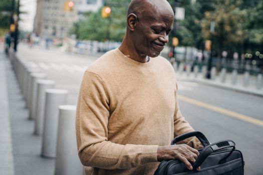 Frowning black businessman with personal case looking inside and grimacing while standing in street