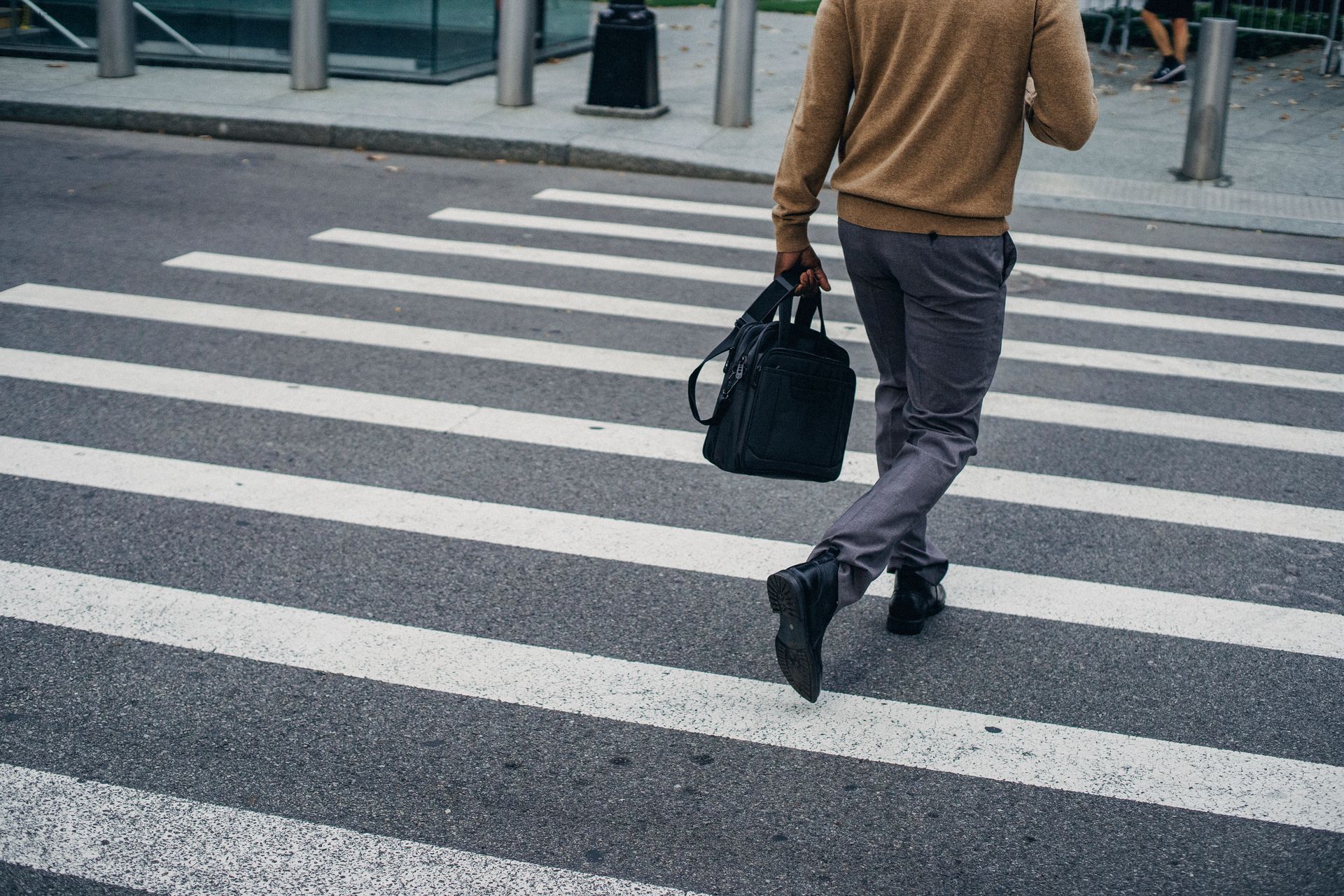 Crop back view of black male pedestrian with bag on crosswalk in city center