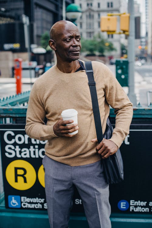 Black man standing near subway entrance with cup of coffee