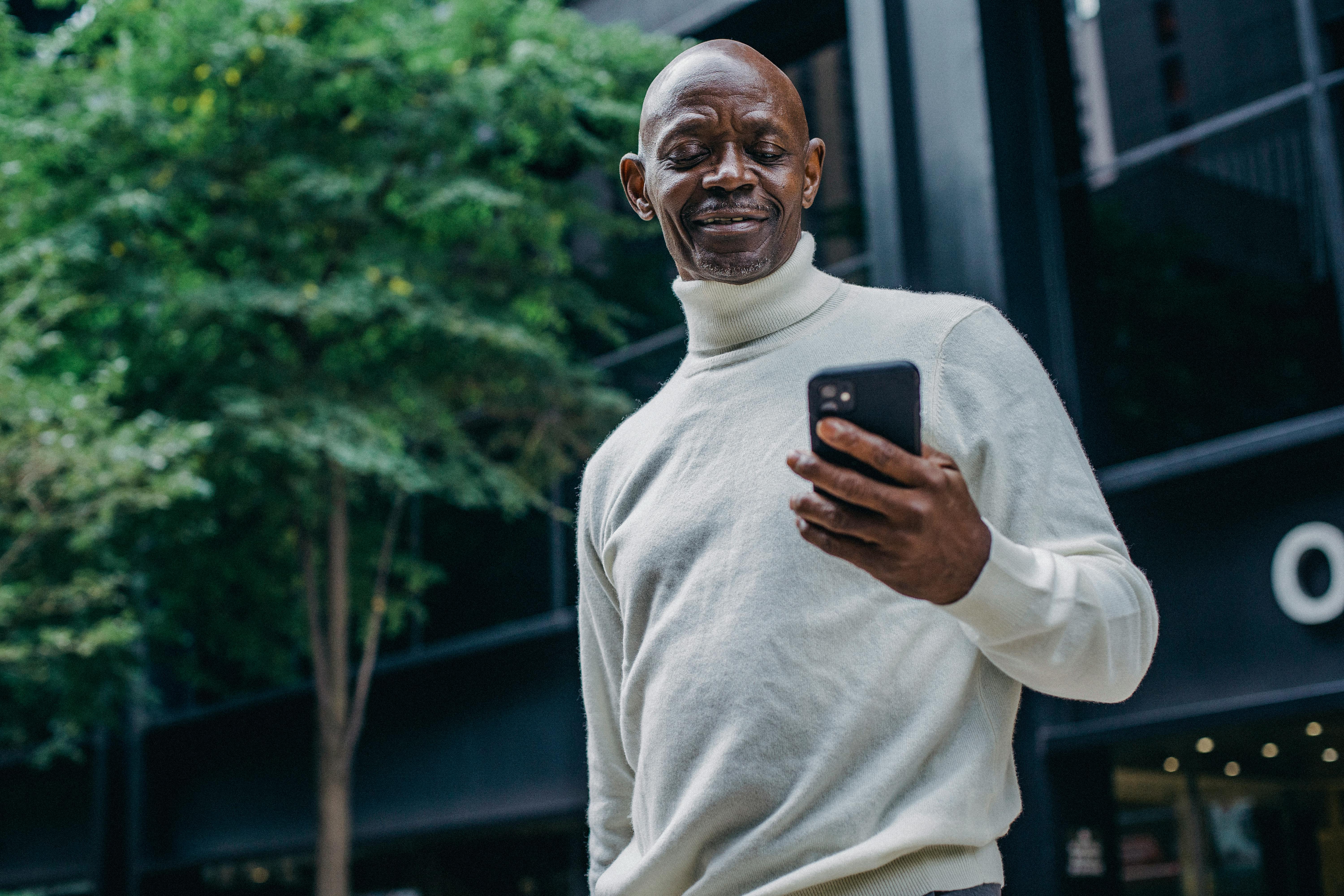 cheerful black man browsing smartphone on street