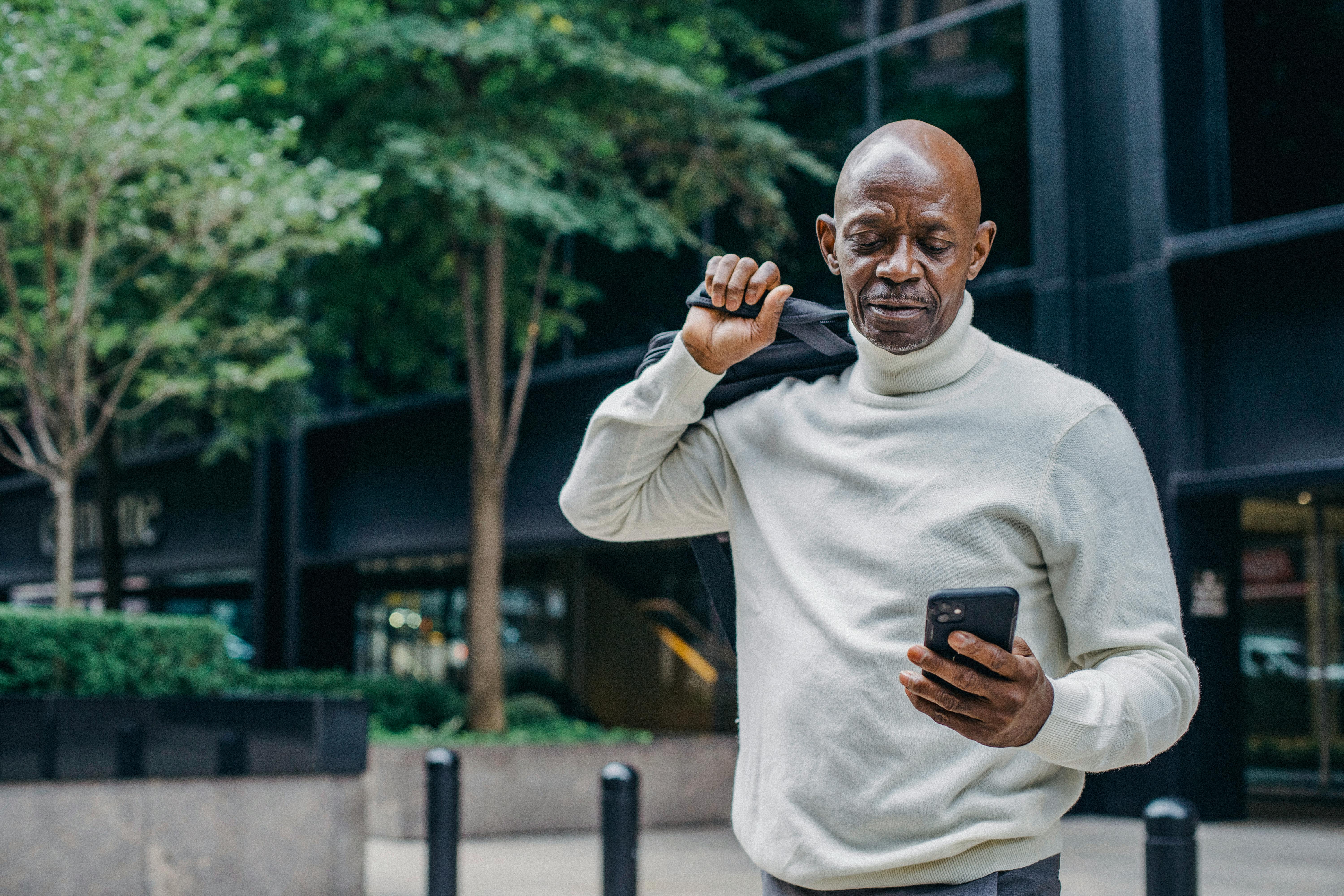 serious black man messaging on smartphone on street