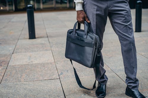 Crop faceless African American businessman in formal clothes with bag standing on pavement street