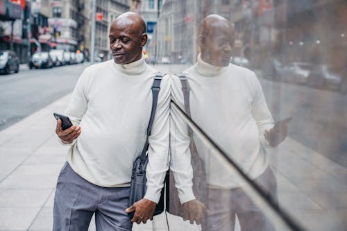 Serious African American man browsing smartphone while leaning on wall in downtown of city