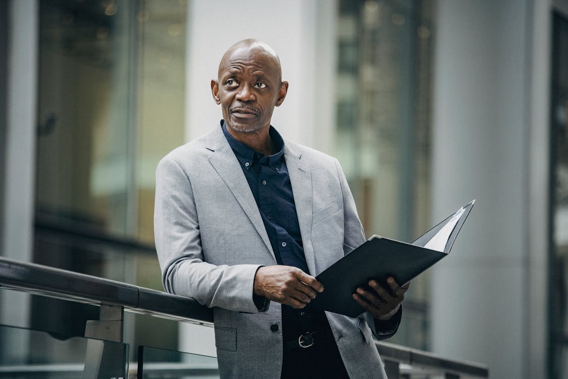 Free Confident African American manager in formal suit carrying folder with papers and looking away in soft daylight Stock Photo