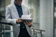 一位穿着正式服装的非裔美国经理，在柔和的白天里，靠在栅栏上阅读重要文件