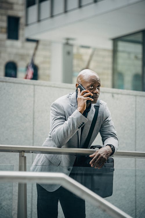 Задумчивый черный предприниматель разговаривает по мобильному телефону и смотрит в сторону
