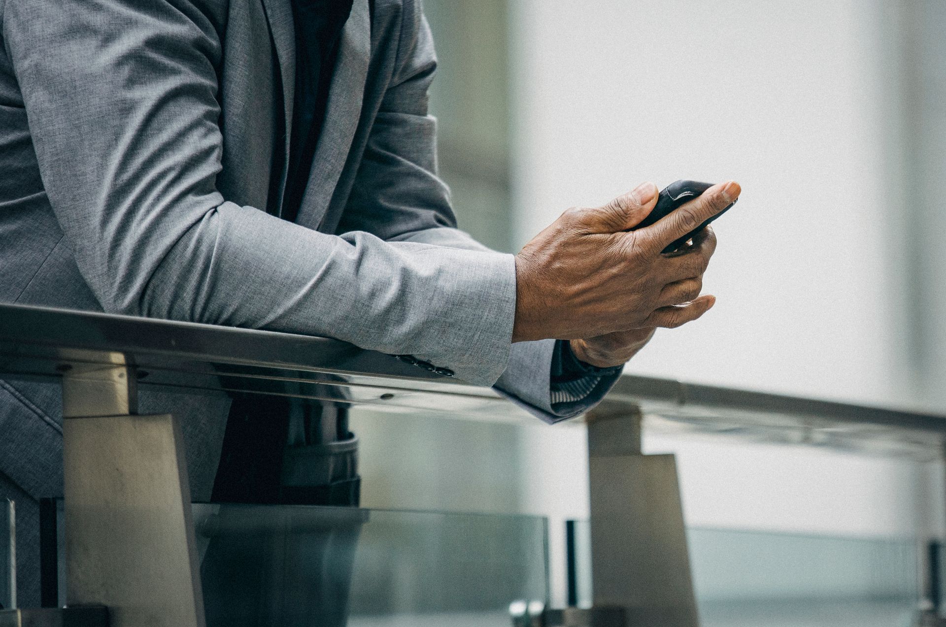 A professional man in a suit texting on a smartphone while leaning on a railing in a city.