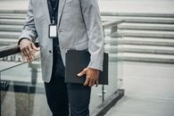 Crop unrecognizable African American entrepreneur leaning on fence and carrying folder with papers in soft daylight
