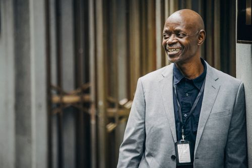 Free Positive African American businessman in formal outfit with authorization card smiling and looking away near modern building in soft daylight Stock Photo