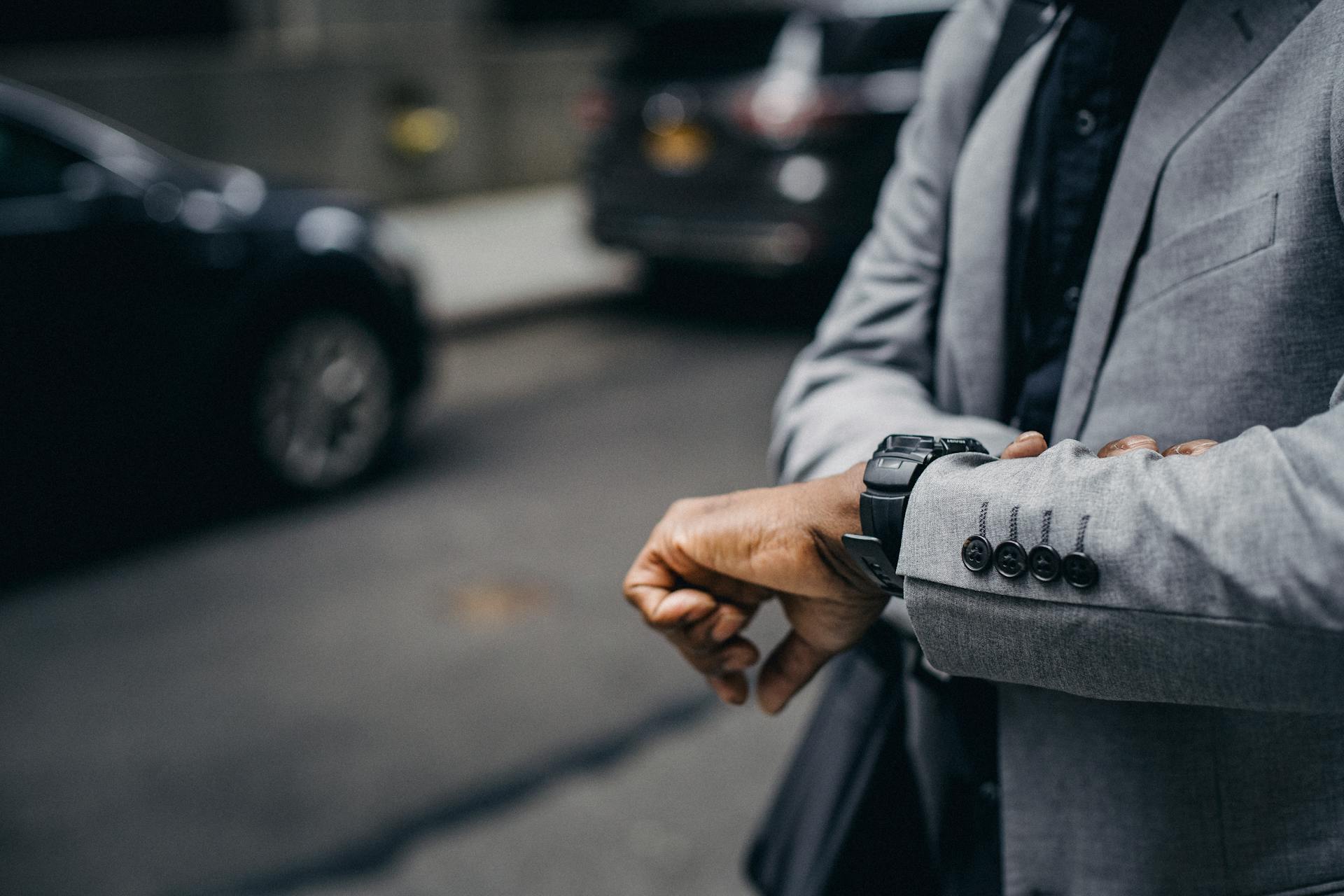 Crop unrecognizable punctual black businessman in formal outfit checking time on sidewalk in modern city