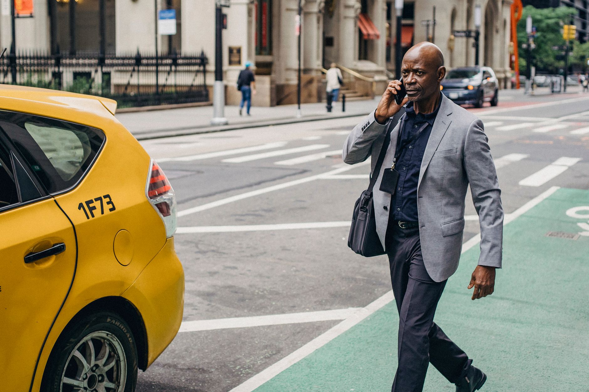Thoughtful adult African American male in classy formal suit having phone call and walking towards taxi car parked on city street