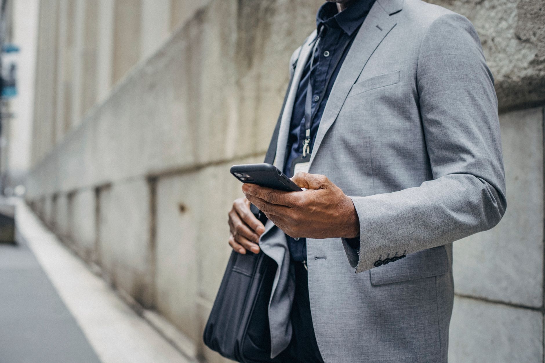 Crop unrecognizable African American male in formal suit standing on street and browsing modern mobile phone