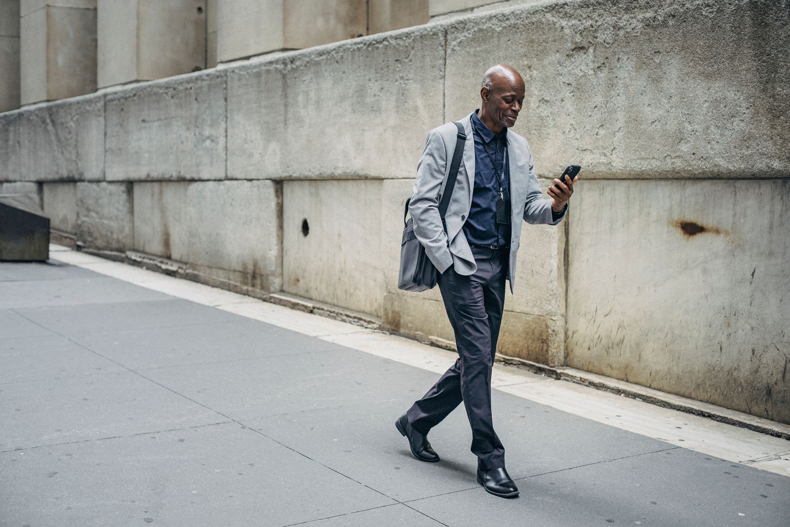 A well-dressed man mid-stride on a city sidewalk, looking down at his phone