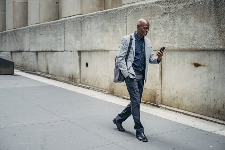 Positive Stylish Black Man Using Smartphone And Walking On Sidewalk