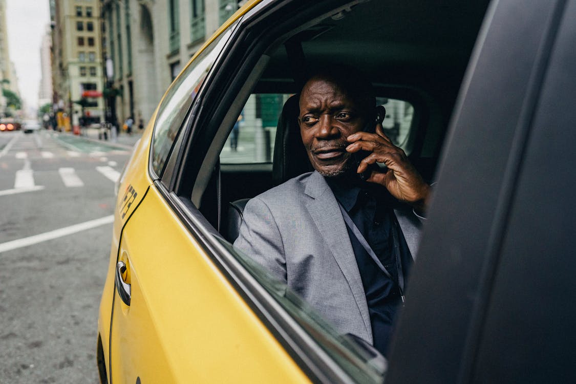 Serious African American male in formal clothes riding taxi on passenger seat and having conversation on mobile phone