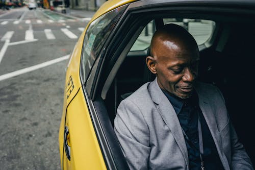 Content African American male wearing formal clothes riding in taxi in back seat and looking down with smile