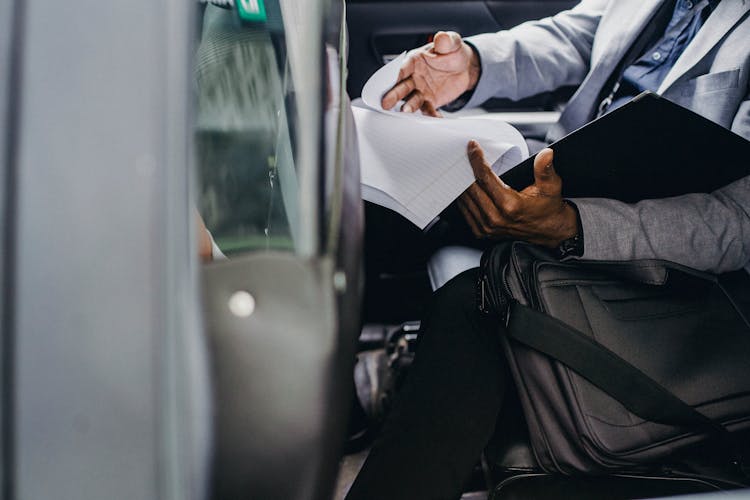 Black Businessman Reading Documents In Folder In Car