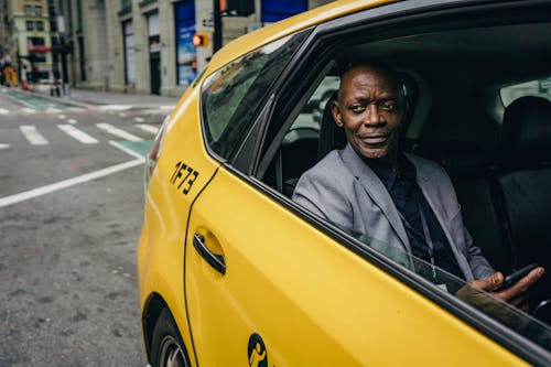 Happy confident mature African American male looking away and expecting important message on mobile phone while sitting in yellow automobile