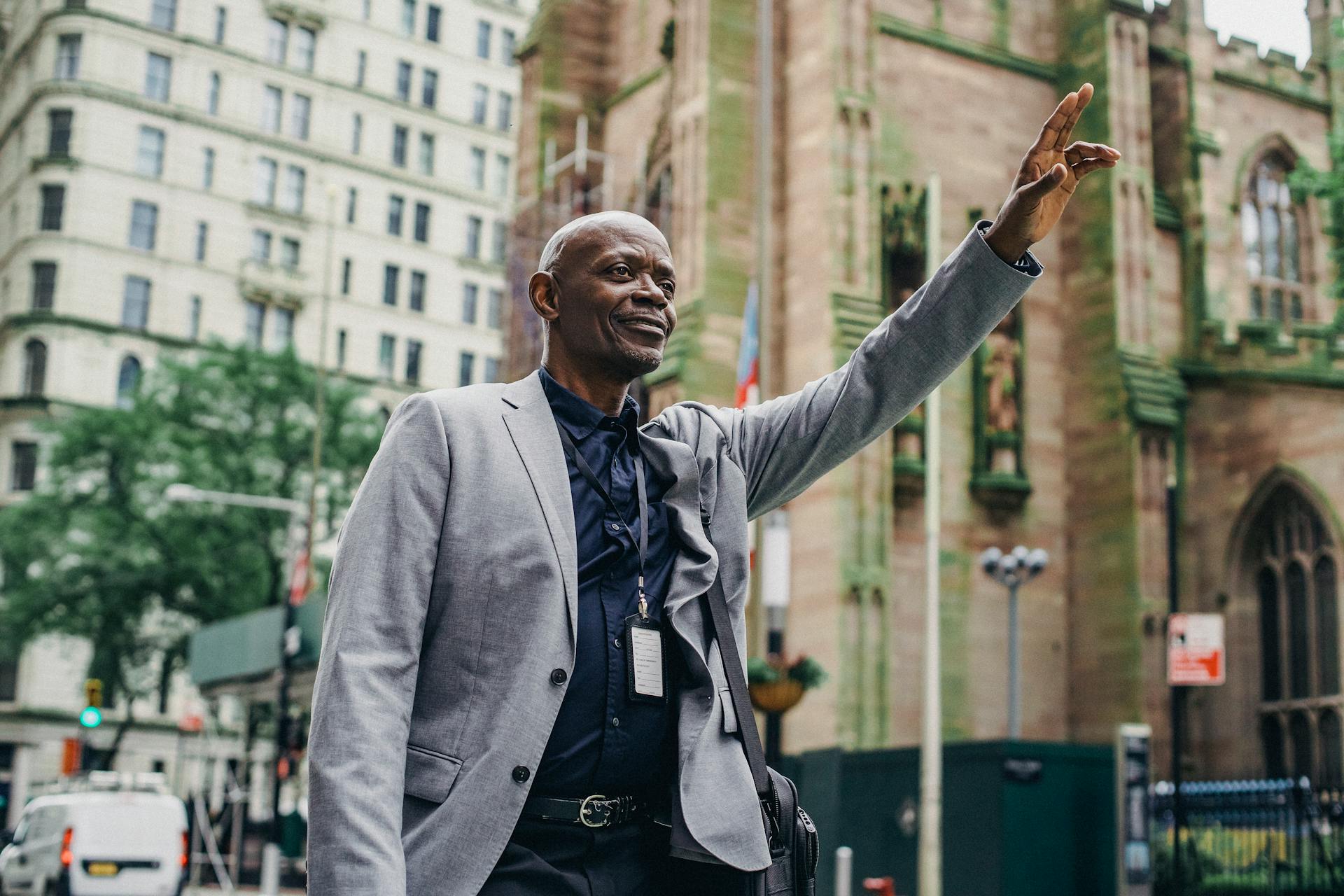 From below of African American male in business suit with hand up on blurred background of buildings