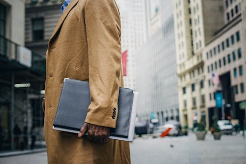 Side view of crop anonymous African American male with folder on blurred background of street