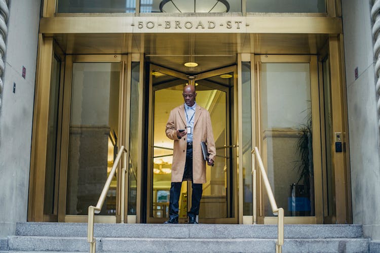 Black Man Receiving Message On Smartphone On Stairs Of Building